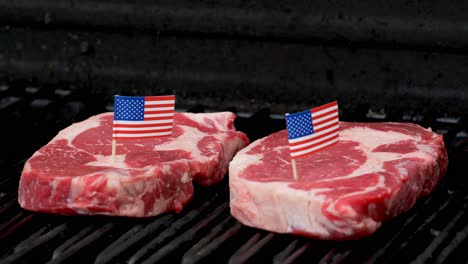 dos bistecs de rib-eye jugosos sentados en la parrilla y cocinados con dos diminutas banderas americanas metidas en ellos