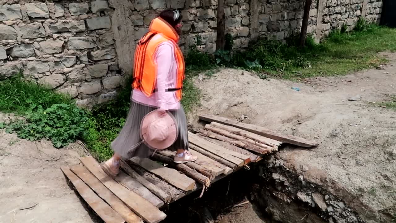 구명조끼를 입은 여성이 허술한 나무다리를 조심스럽게 건너고 있다.