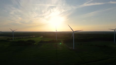 Grandes-Turbinas-Eólicas-Con-Palas-En-El-Campo-Vista-Aérea-Puesta-De-Sol-Naranja-Brillante-Cielo-Azul-Parque-Eólico-Giro-De-Drones-En-Cámara-Lenta