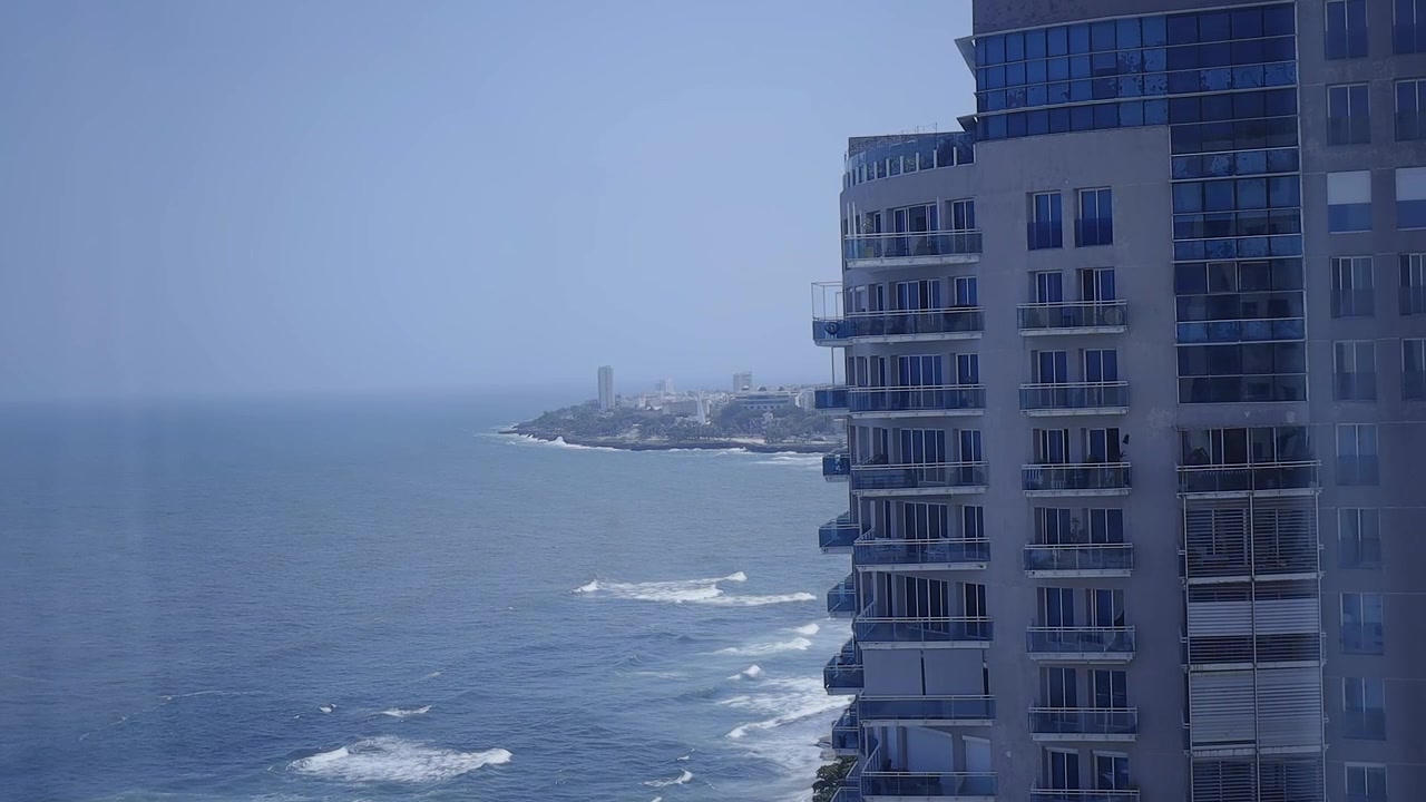 Um moderno edifício de apartamentos arranha-céu ergue-se imponente contra o pano de fundo do oceano azul e do horizonte da cidade