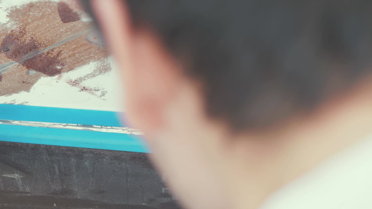 hombre caucásico aplicando cinta de pintura al casco de un barco de madera, de cerca