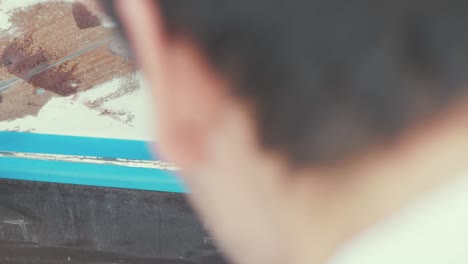 hombre caucásico aplicando cinta de pintura al casco de un barco de madera, de cerca