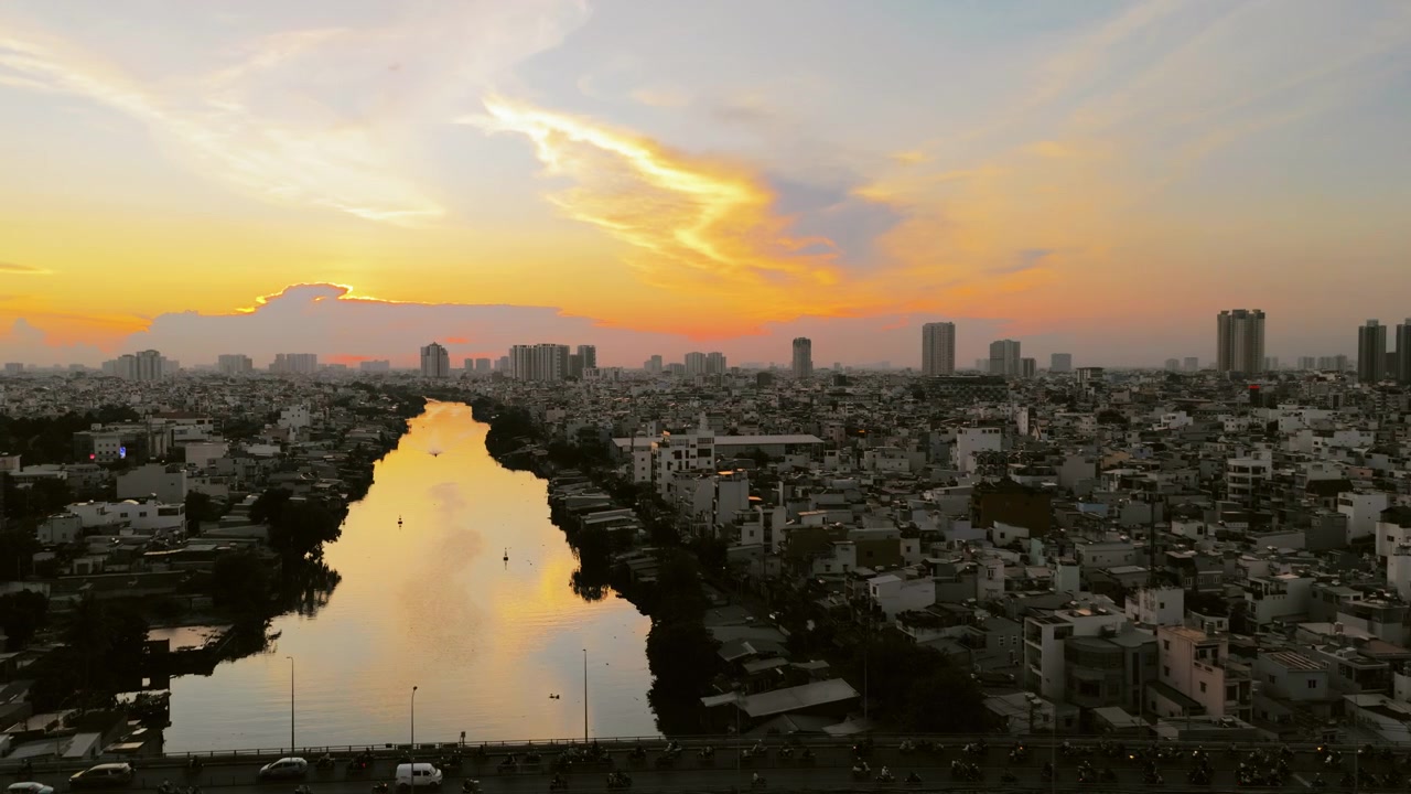 Ho Chi Minh Şehri'ndeki bir nehrin üzerinde gün batımının güzel kuş bakışı görünümü. Yoğun şehir silüetinin üzerinde turuncu gökyüzü parıldarken altın rengi ışık suya yansıyor