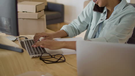 joven negra sentada en el escritorio, trabajando en la computadora y revisando el pedido por teléfono