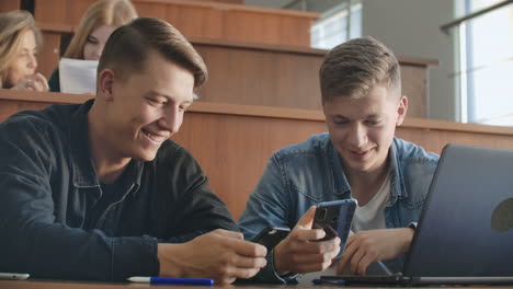 Male-students-with-a-smartphone-in-their-hands-laughing-in-the-audience-during-a-break-for-a-lecture-at-the-University.