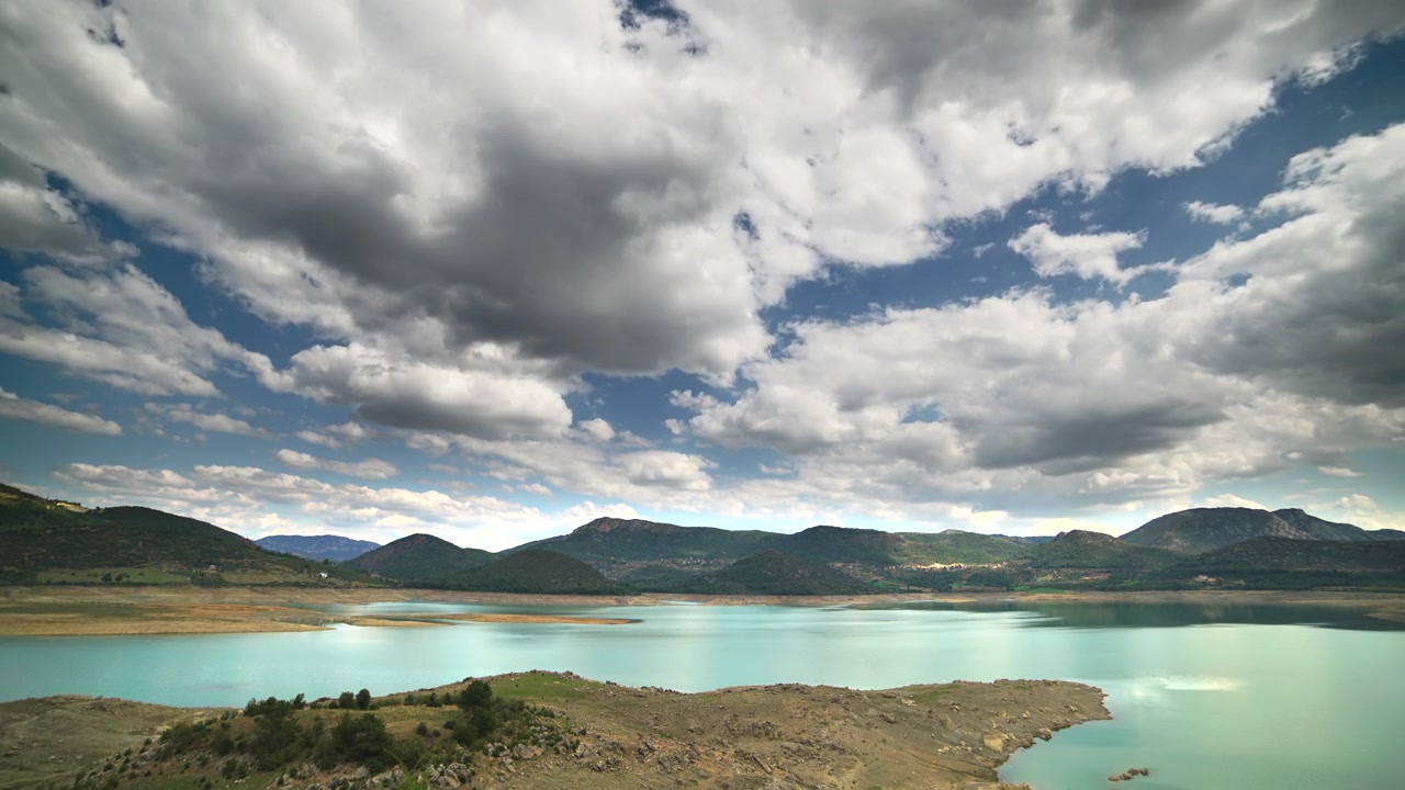Vista Panoramica di un Lago Turchese Circondato da Montagne e Nuvole
