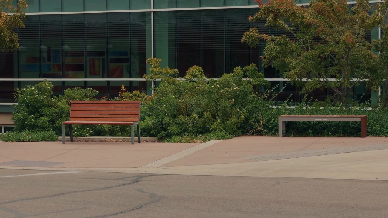 A right-to-left glide reveals two benches, shrubs, and a glass-fronted building.
