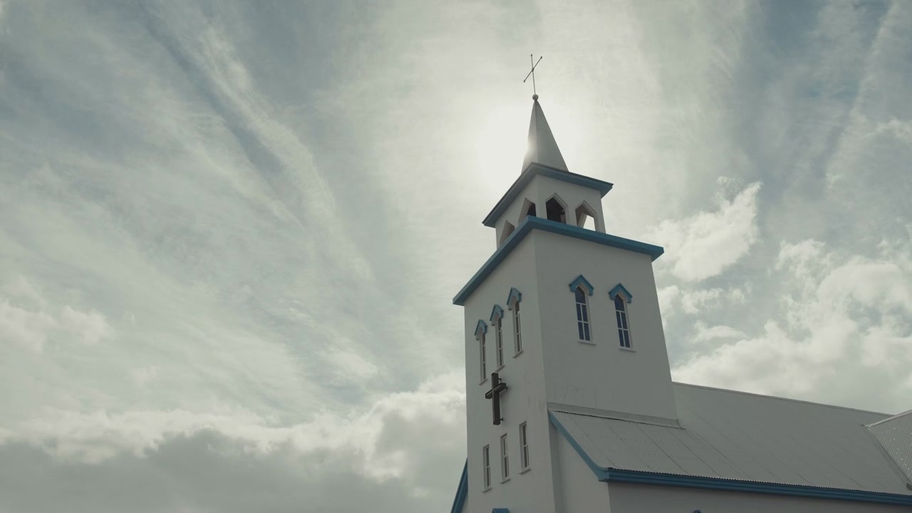 Campanile bianco di chiesa con croce contro il sole splendente e nuvole in movimento