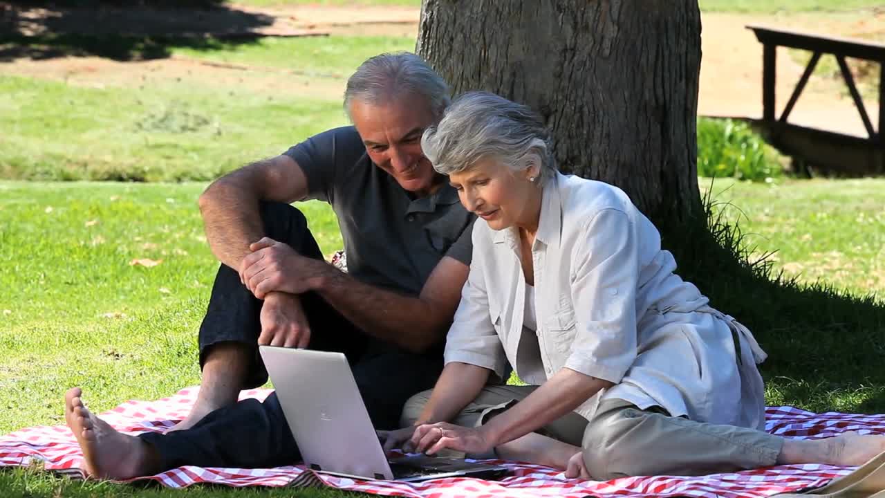 Senior couple looking at a laptop sitting on a tablecloth