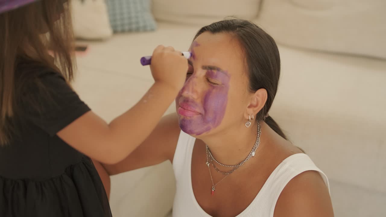 niña con sombrero de bruja aplicando maquillaje a su madre embarazada para halloween