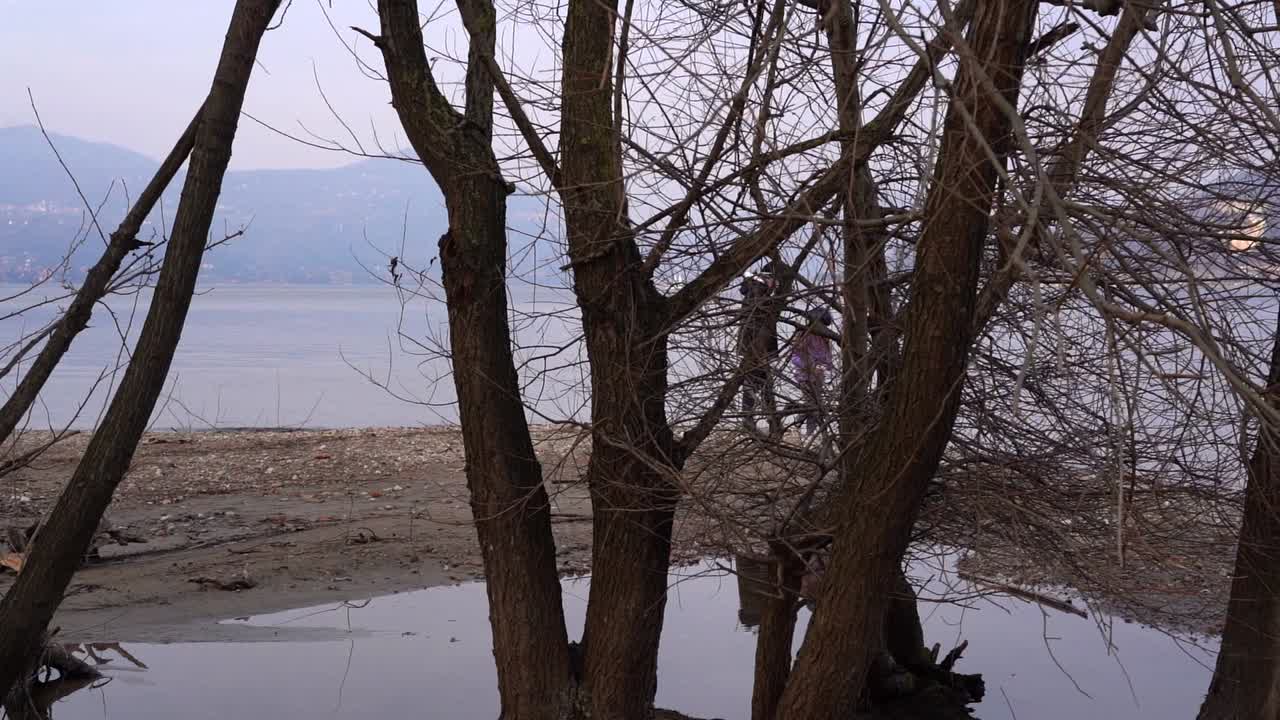 Disquieting shot of mother and child seen through trees on lakeside