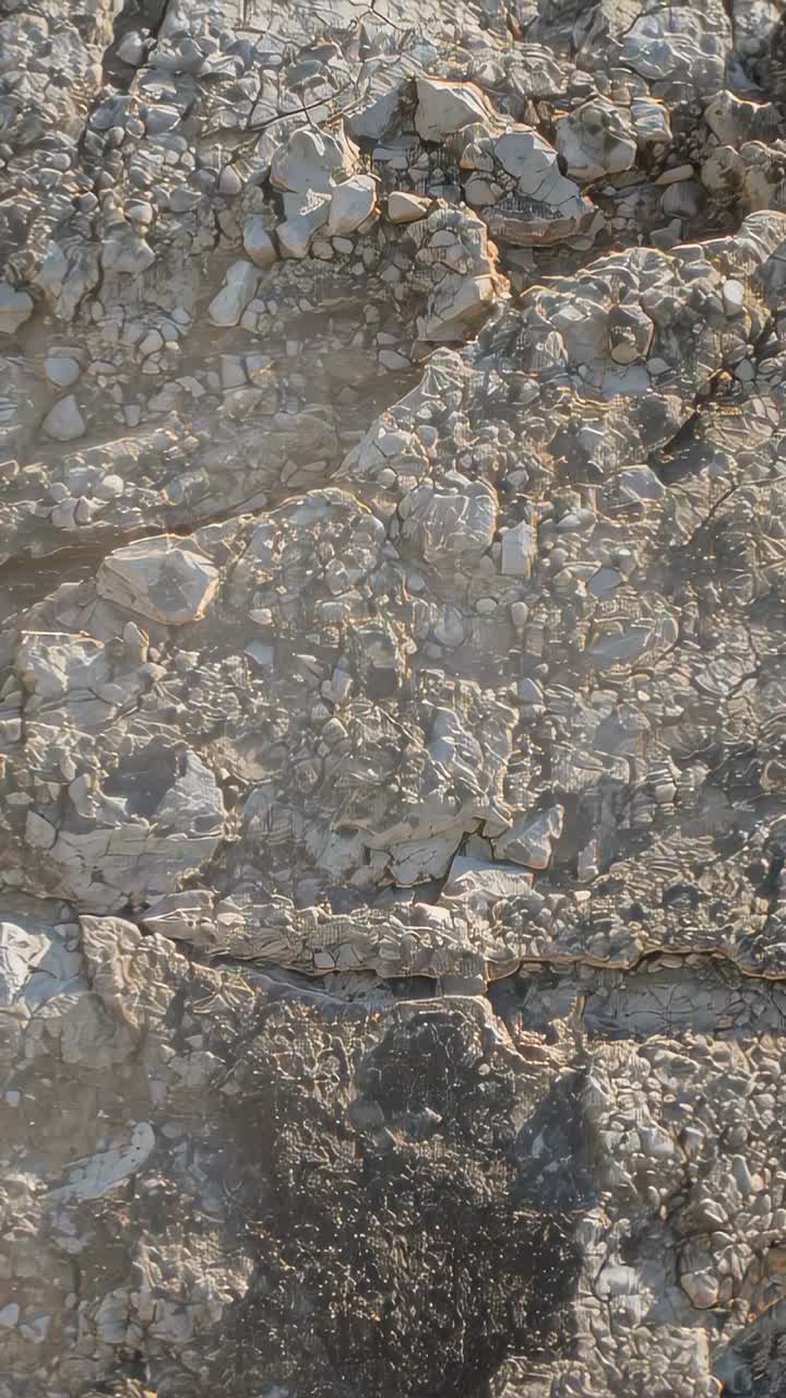 Video verticale: Telecamera che panoramica dopo una spinta della mano, spostandosi su un affioramento roccioso e centrando una macchia più scura