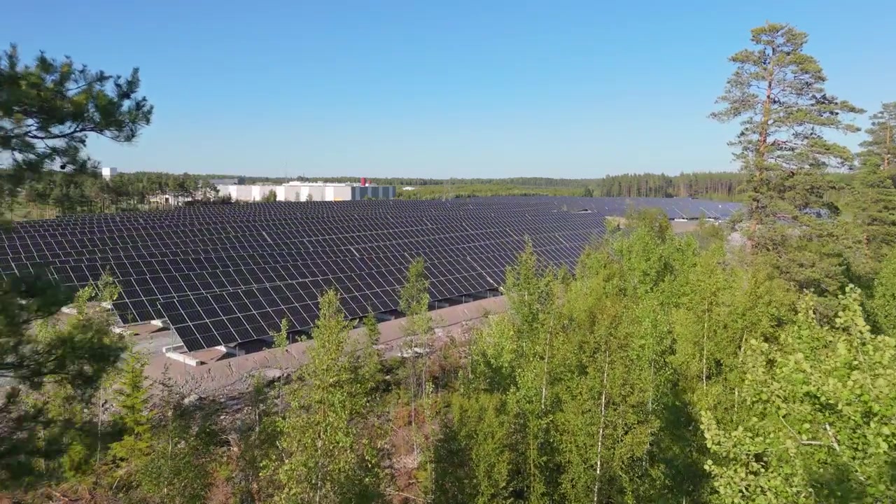Bredt luftfoto med dolly-bevægelse gennem træer af en solcellepark i Finland med bifaciale solpaneler, der producerer ren energi.