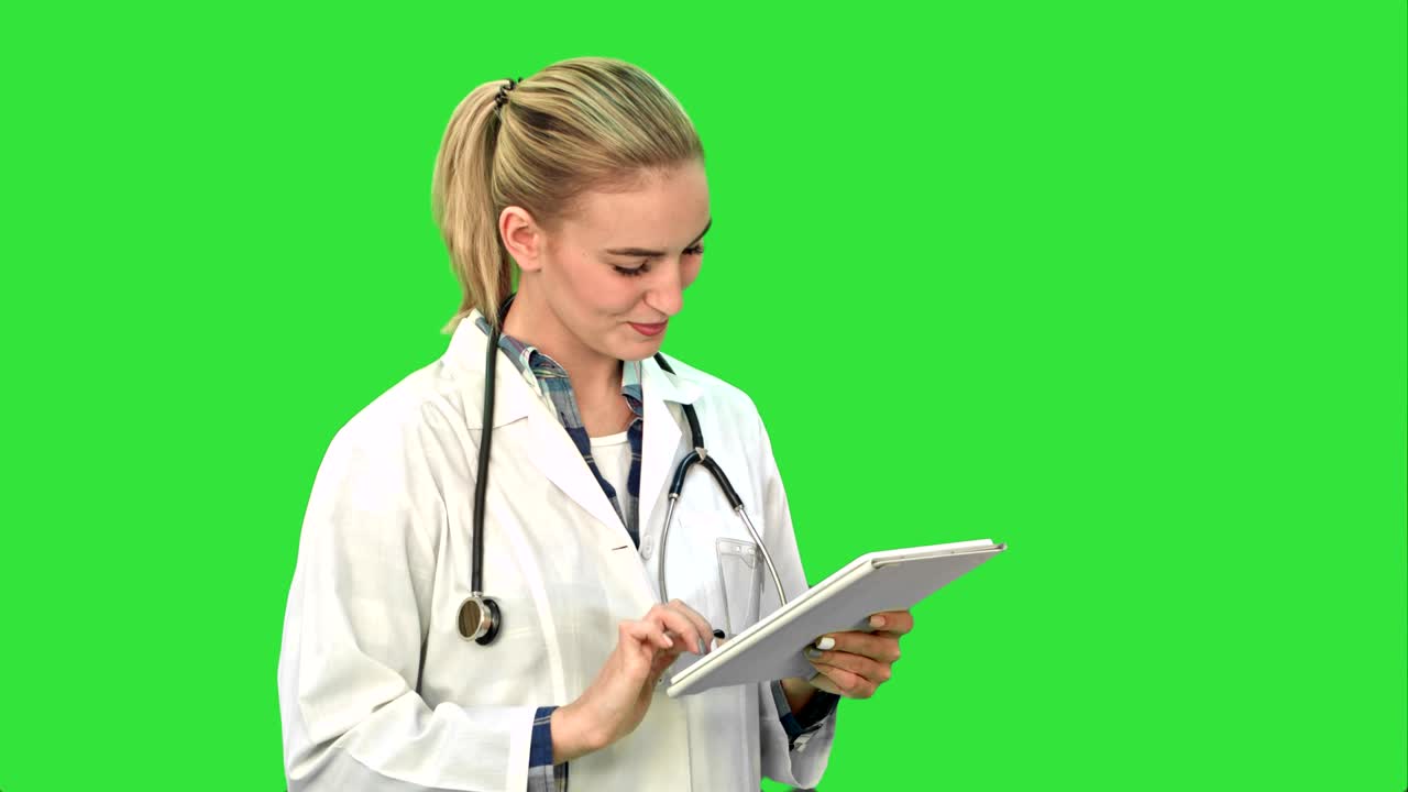 Affascinante dottoressa con stetoscopio che sorride mentre usa un tablet su schermo verde, Chroma Key.