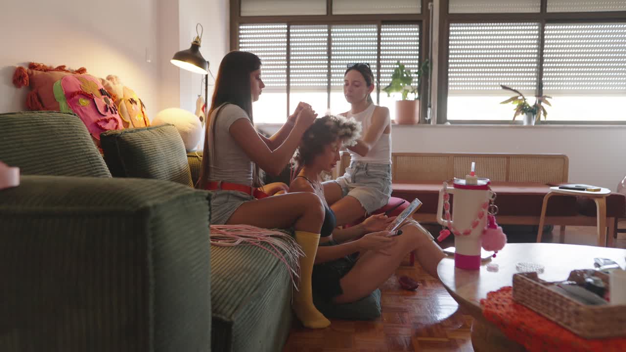Two women braiding a friend's hair indoors