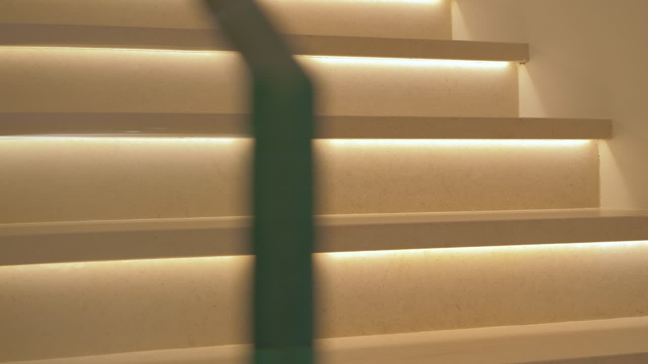 toma panorámica que revela escaleras blancas brillantemente iluminadas con un riel de vidrio dentro de una mansión