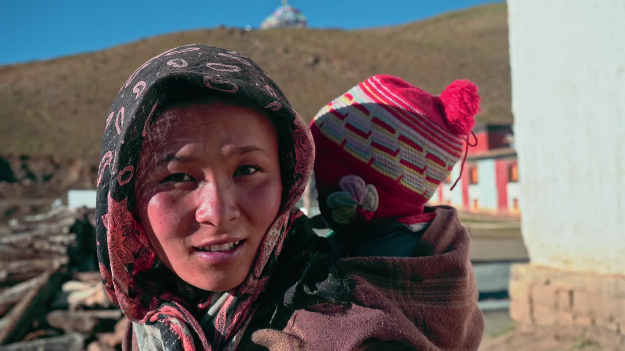 Smiling Portrait of an Indian Himachali mother carrying her child at the back in the mountain region of spiti valley.