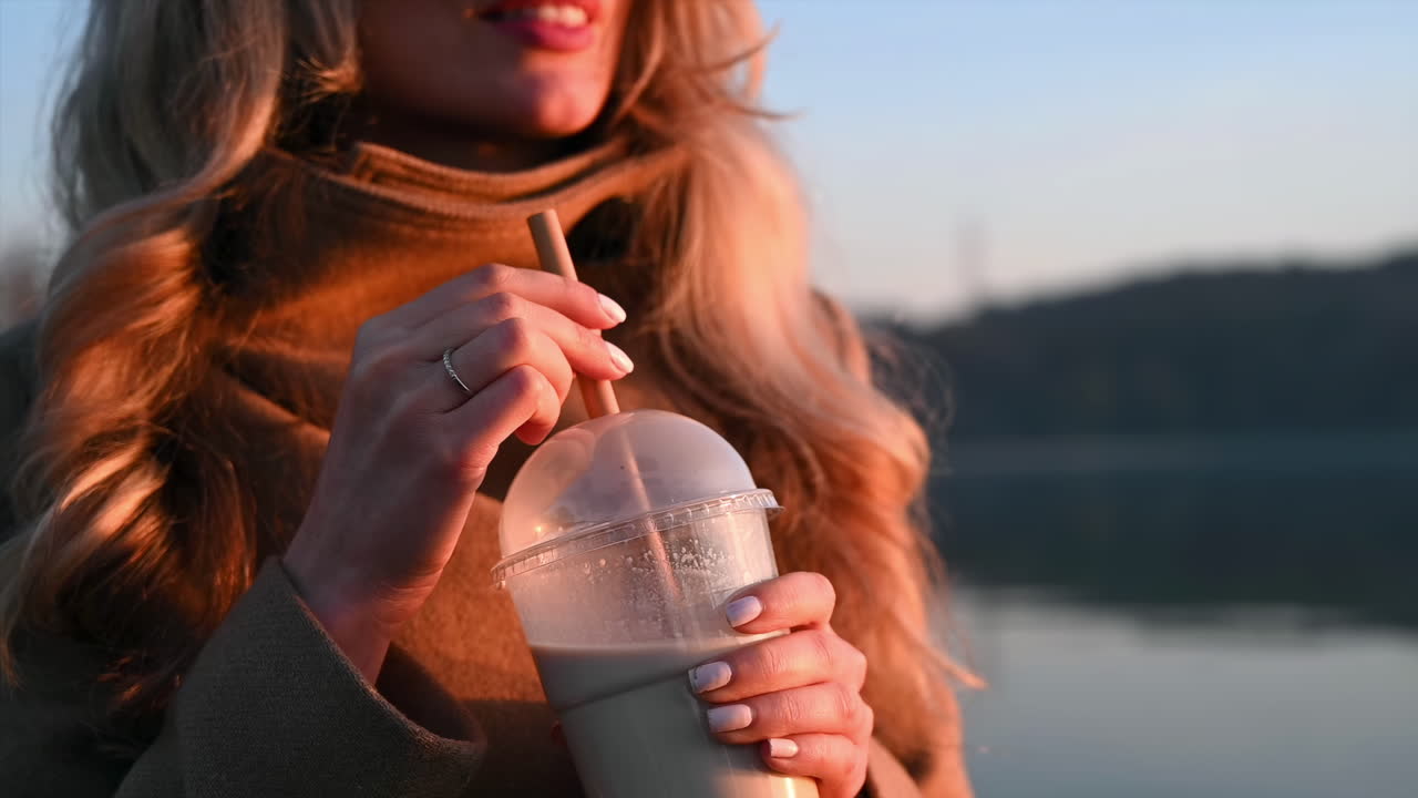 Young woman mix coffee with a bamboo straw and smile at sunset