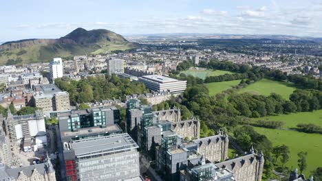 Curve-panning-shot-over-Edinburgh-University-buildings-and-the-Meadows,-towards-Arthurs-Seat,-on-a-sunny-day-|-Edinburgh,-Scotland-|-4K-at-30-fps