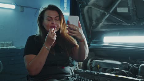 woman mechanic taking a selfie while applying lipstick in a garage