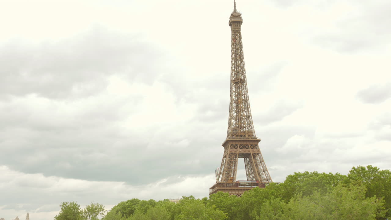 에펠 탑의 부분은 구름이 많은 날 바닥에 있는 나무와 함께 높이 서 있습니다.