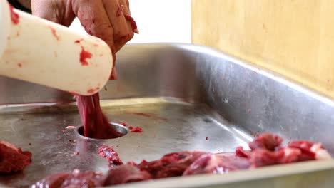 Butcher-holding-a-plastic-plunger-while-pushing-chunks-of-wild-game-meat-into-hopper-of-a-meat-grinder