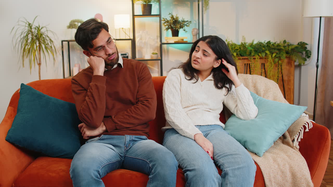 Upset stressed indian couple man woman sitting on sofa talking discussing in living room at home