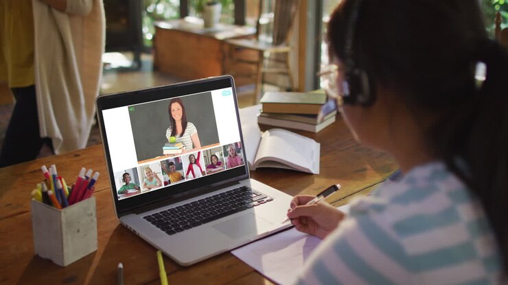 Scolara che usa il laptop per una lezione online a casa, con un'insegnante di diverse origini e la classe sullo schermo