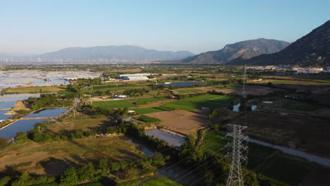 Enormes-Campos-De-Sal-Entre-La-Naturaleza-Verde-Y-Las-Altas-Montañas-En-Vietnam,-Donde-Los-Modernos-Postes-De-Electricidad-Atraviesan-El-área-En-Phan-Rang-Vietnam