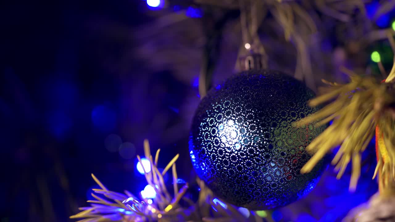 Round Christmas toy on winter holidays. Beautiful blue christmas ball on New Year tree on blur blinking background. Close-up.
