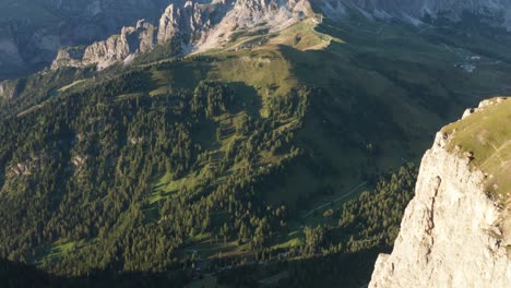 Aerial-tilt-up-shot-of-green-plateau-in-Val-Gardena-Pass,-featuring-mountain-range-of-Puez-Odle-during-golden-hour