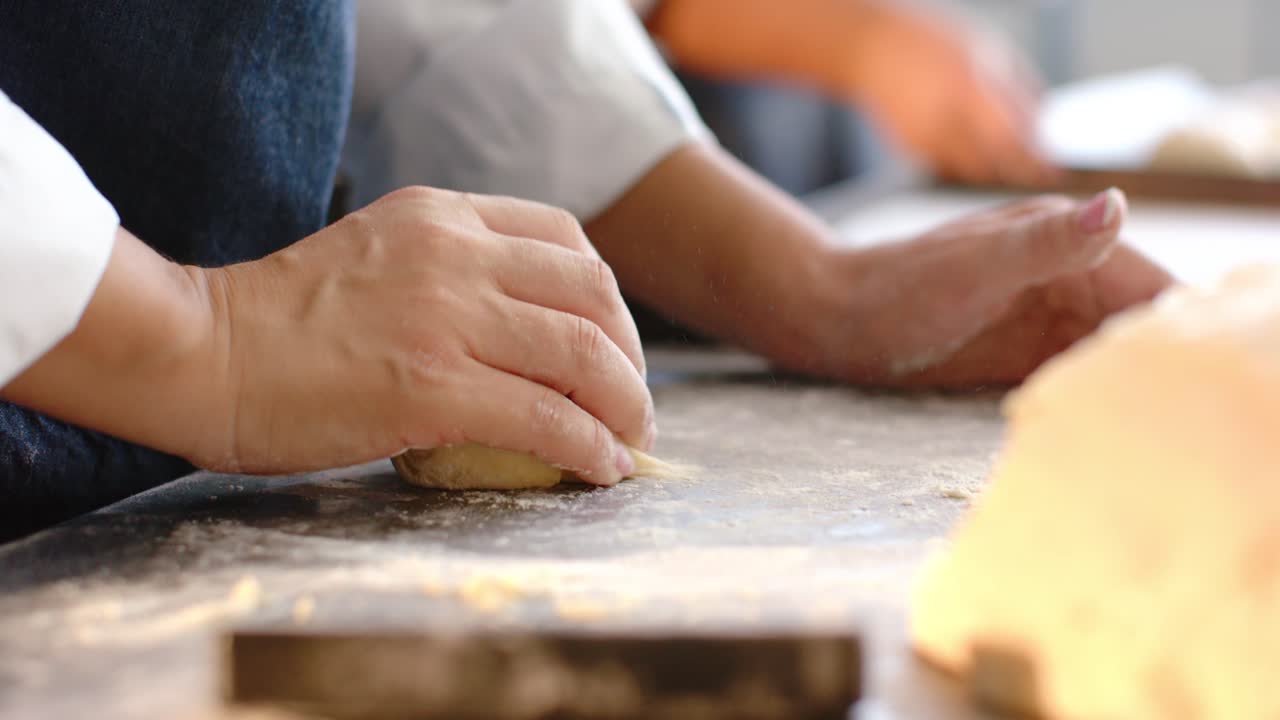 Diverse aproned bakers sprinkling flour, pressing dough on bench with scraper, preparing for baking