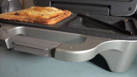 cooked ham and cheese toasty is removed from the sandwich maker