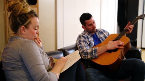 man playing guitar while woman reading book