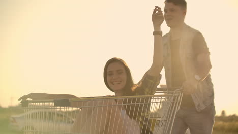 Linseneffekt:-Fröhliches-Paar,-Mann-Und-Frau,-Fährt-Bei-Sonnenuntergang-In-Zeitlupe-Mit-Einkaufswagen-Im-Supermarkt.