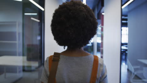 mujer de negocios biracial caminando y bebiendo una taza de café en una oficina moderna