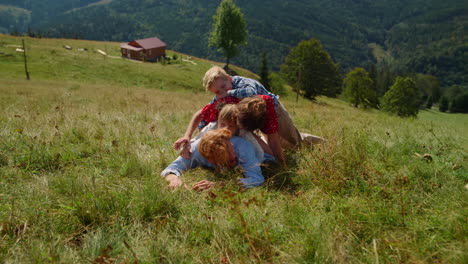 happy family lying piled top each other on green hill. couple playing with kids.