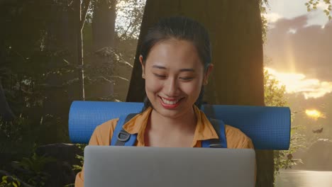 close up of asian female hiker with mountaineering backpack using a laptop while exploring forest nature