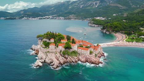 drone circling around sveti stefan island in montenegro. panoramic aerial view of all region. luxury travel destination. waves breaking on the rock. mountains in background