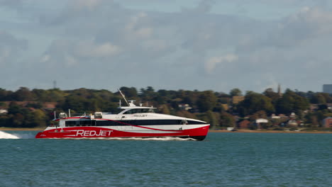 panning shots of red jet powered catamaran ferry on the solent in southampton with weston in background