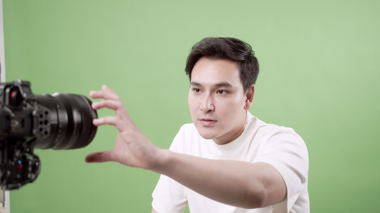 A young male creator is seen preparing for his video shoot by checking camera angles and adjusting his appearance, ready to deliver engaging content with a green background.