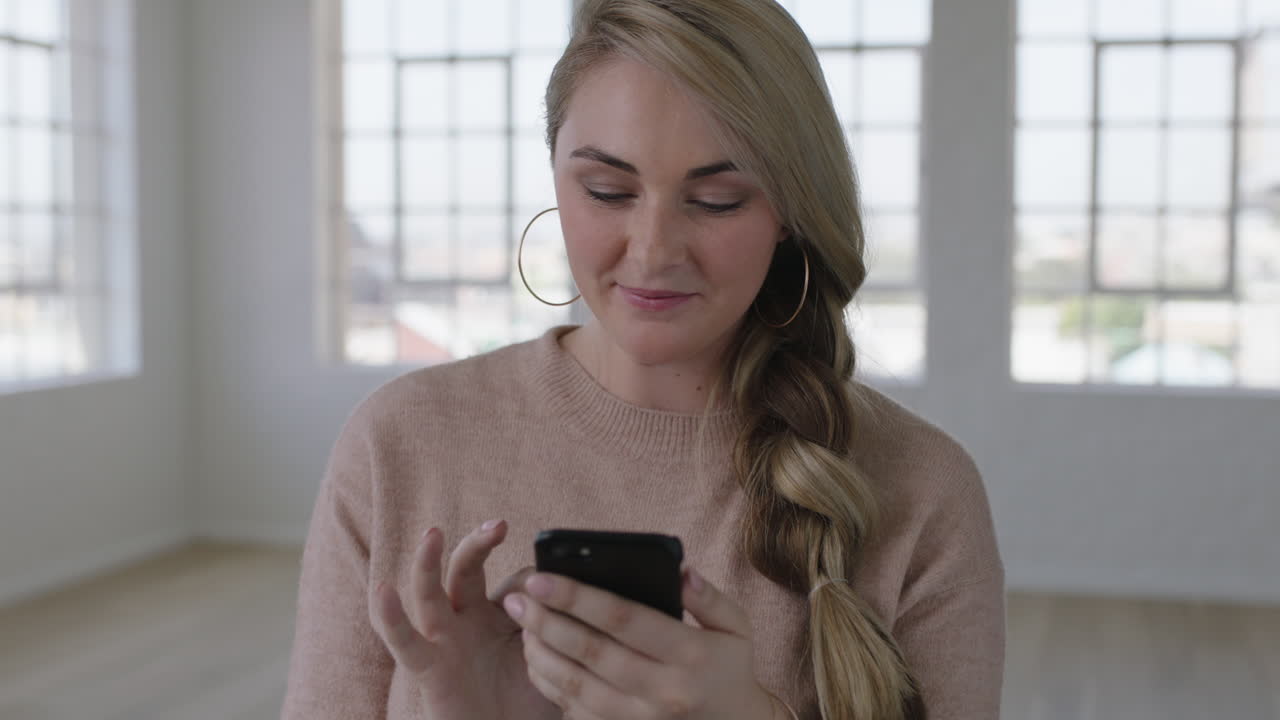 ritratto di una bella giovane donna bionda che usa uno smartphone, scrive messaggi, naviga, gode della tecnologia mobile sullo sfondo di un appartamento