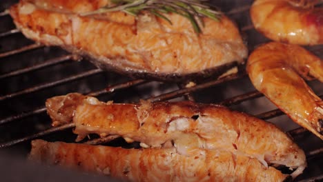 chef cooking red salmon fish steaks with oil and spices on grill close-up. prawns on fire throwing them on pan. making dorado fishes on frying grill. restaurant food concept. sea food barbecue.