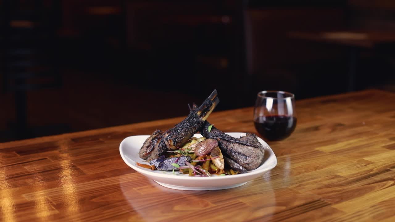 맛있는 구운 양갈비 한 접시가 나무 테이블에 적포도주 한 잔과 함께 제공됩니다.