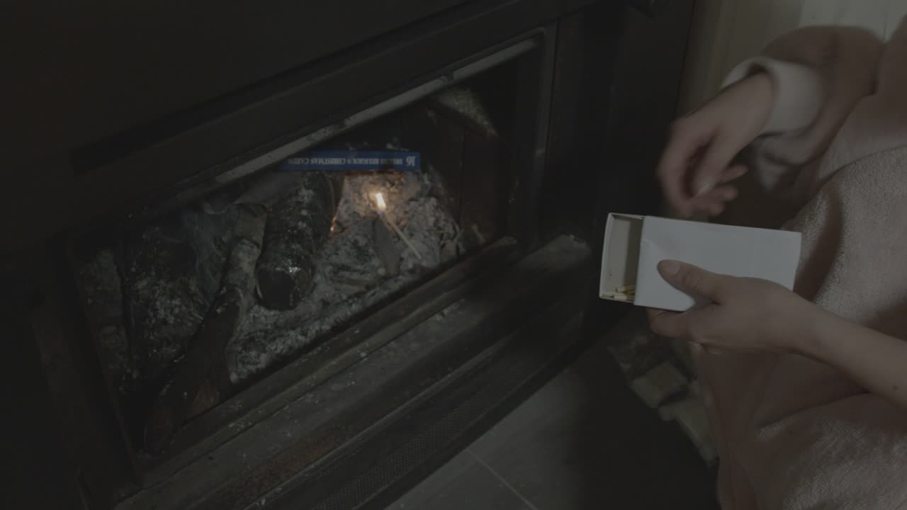A young girl, dressed warmly, carefully lights a fireplace in a dimly lit, cozy room. The gentle glow casts soft shadows, creating a warm, inviting ambiance in this intimate interior setting
