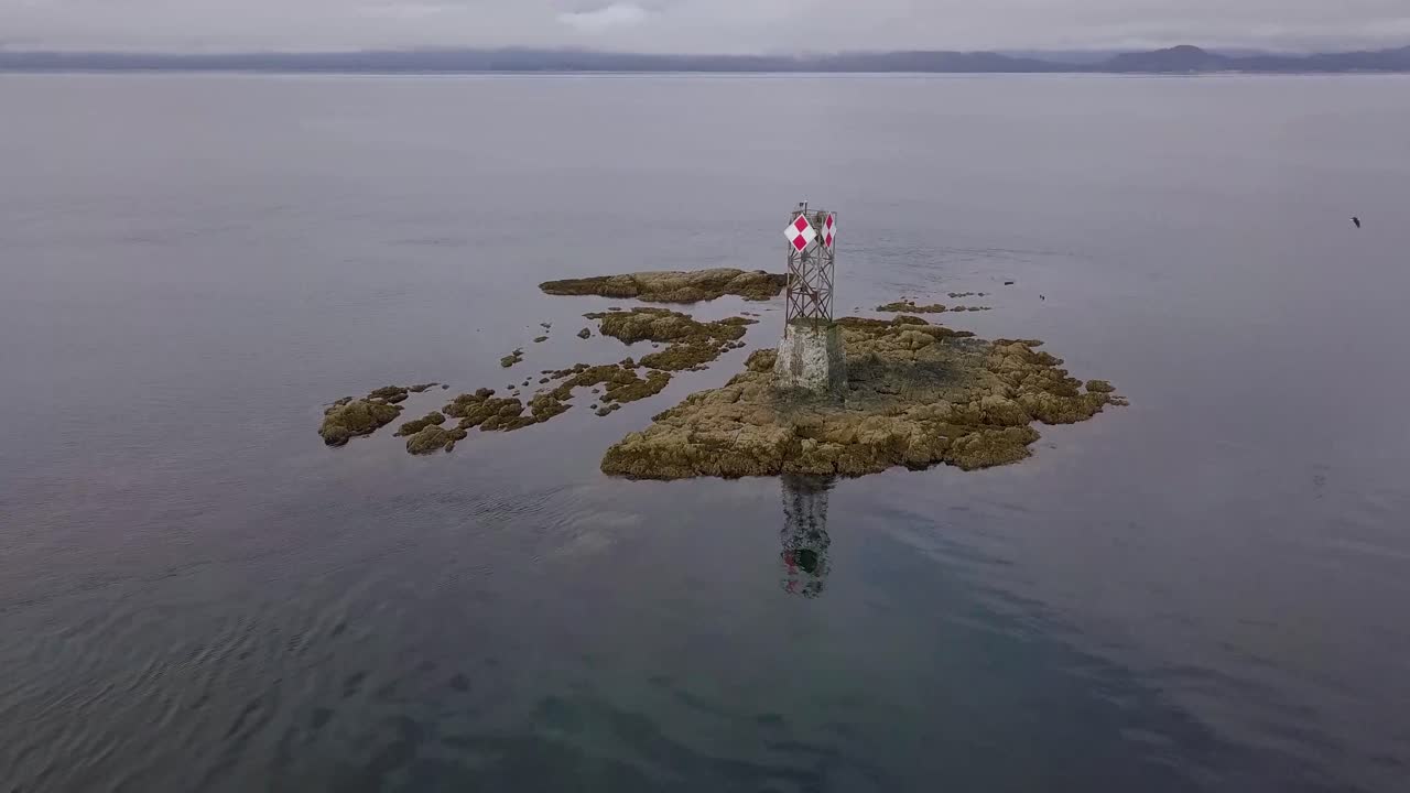 flotando en el aire lejos del arrecife de vanderbilt y la baliza de navegación a medida que la gaviota vuela lejos, el océano y las montañas de alaska detrás