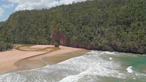 aerial pullback shot of tropical rainforest with sandy beach and waves of ocean - river mouth connecting sea and stream - establishing drone shot in paradise