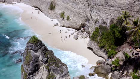 People-bathing-on-Diamond-Beach-in-Nusa-Penida-island-Indonesia-behind-rock-spire-structure,-Aerial-pedestal-up-reveal-shot