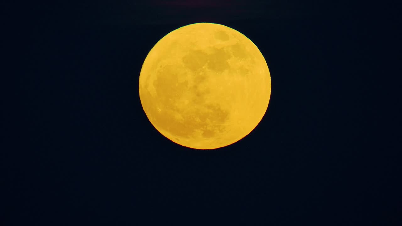 Superlua azul cheia com matiz de gradiente amarelo-laranja contra o céu preto escuro, brilho suave.