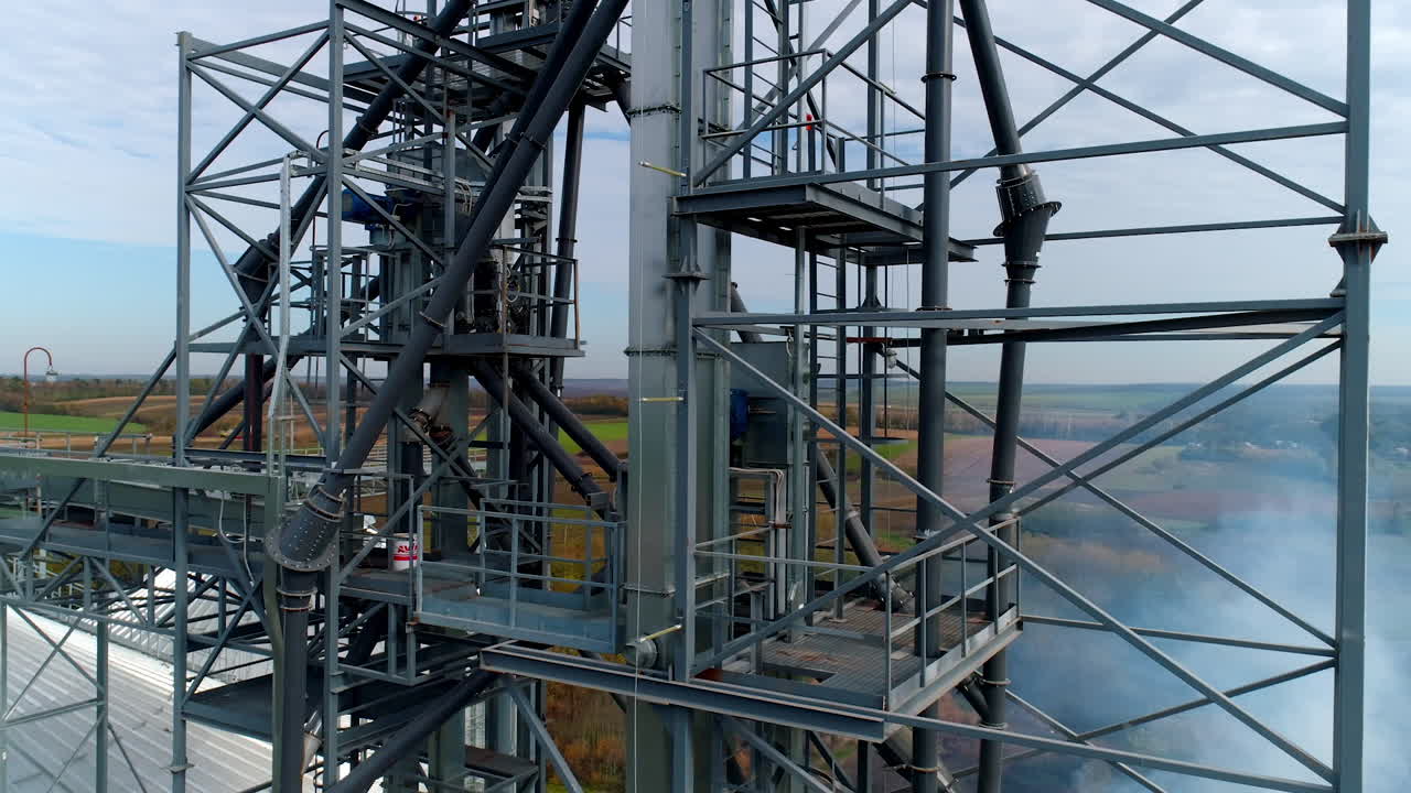Manufacturing in the countryside. Steel frame of a modern plant on nature background. Harmful smoke released into the air from industrial factory. Aerial view.